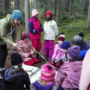 Leirivastaava ja joukko lapsia metsässä tutkimusretkellä